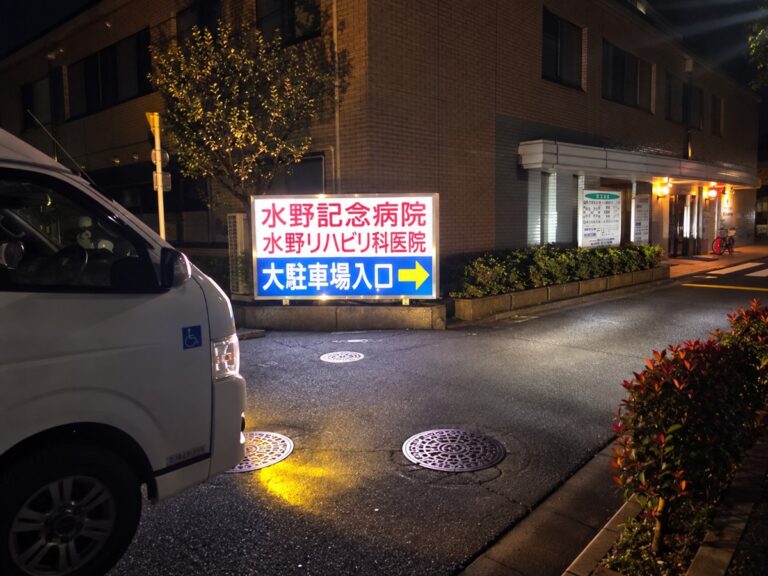 水野記念病院（足立区西新井）の夜間の駐車場入口と、前に停まる車いす対応の介護タクシー